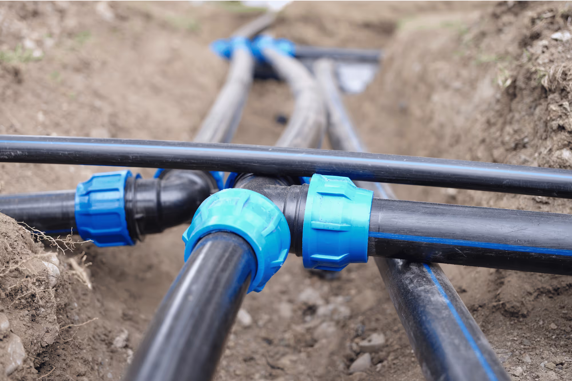 Underground water pipe installation with black HDPE pipes and blue compression fittings for a sanitary water system.
