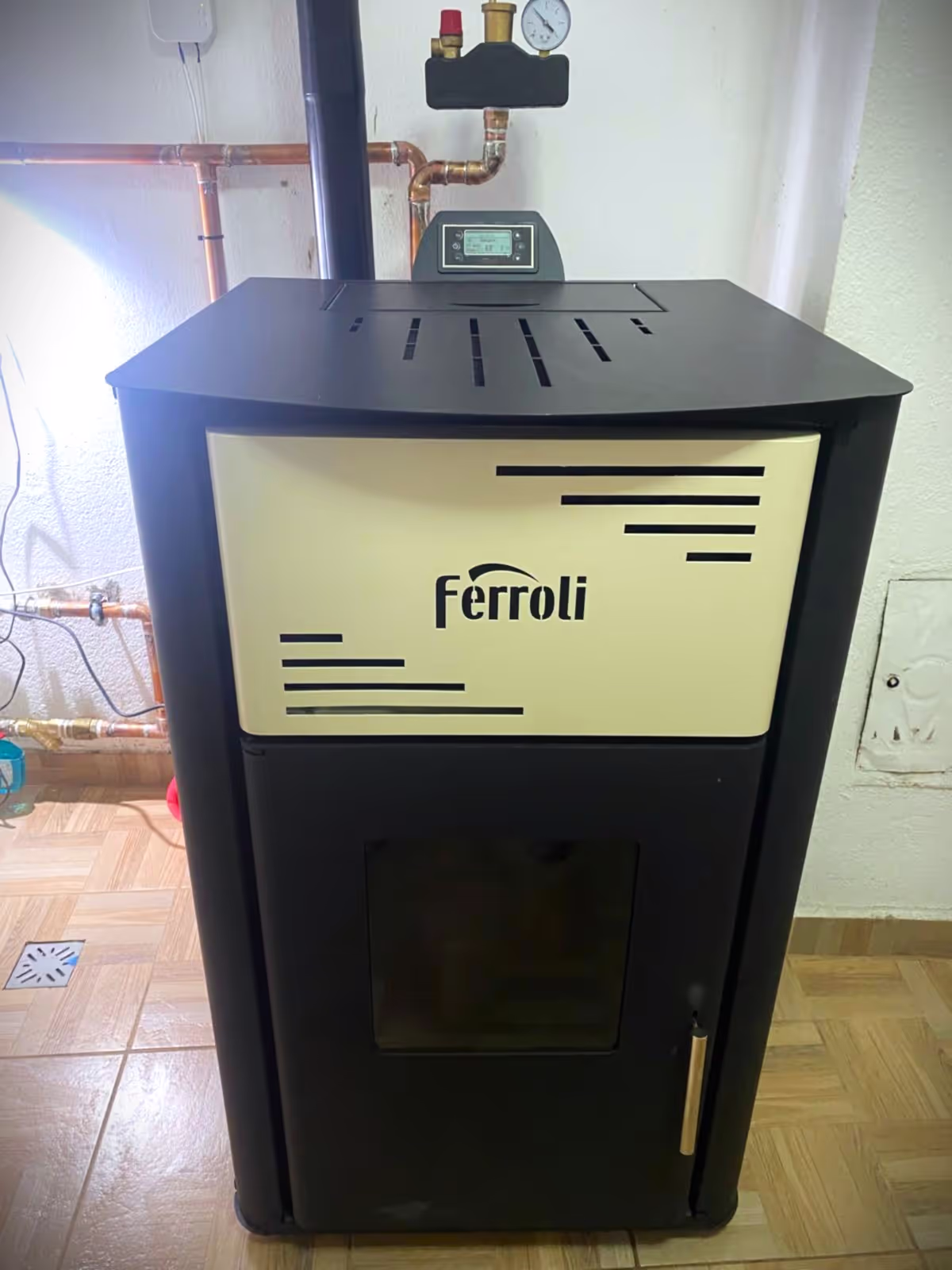 A Ferroli heating stove installed indoors with connected pipes and a digital control panel.