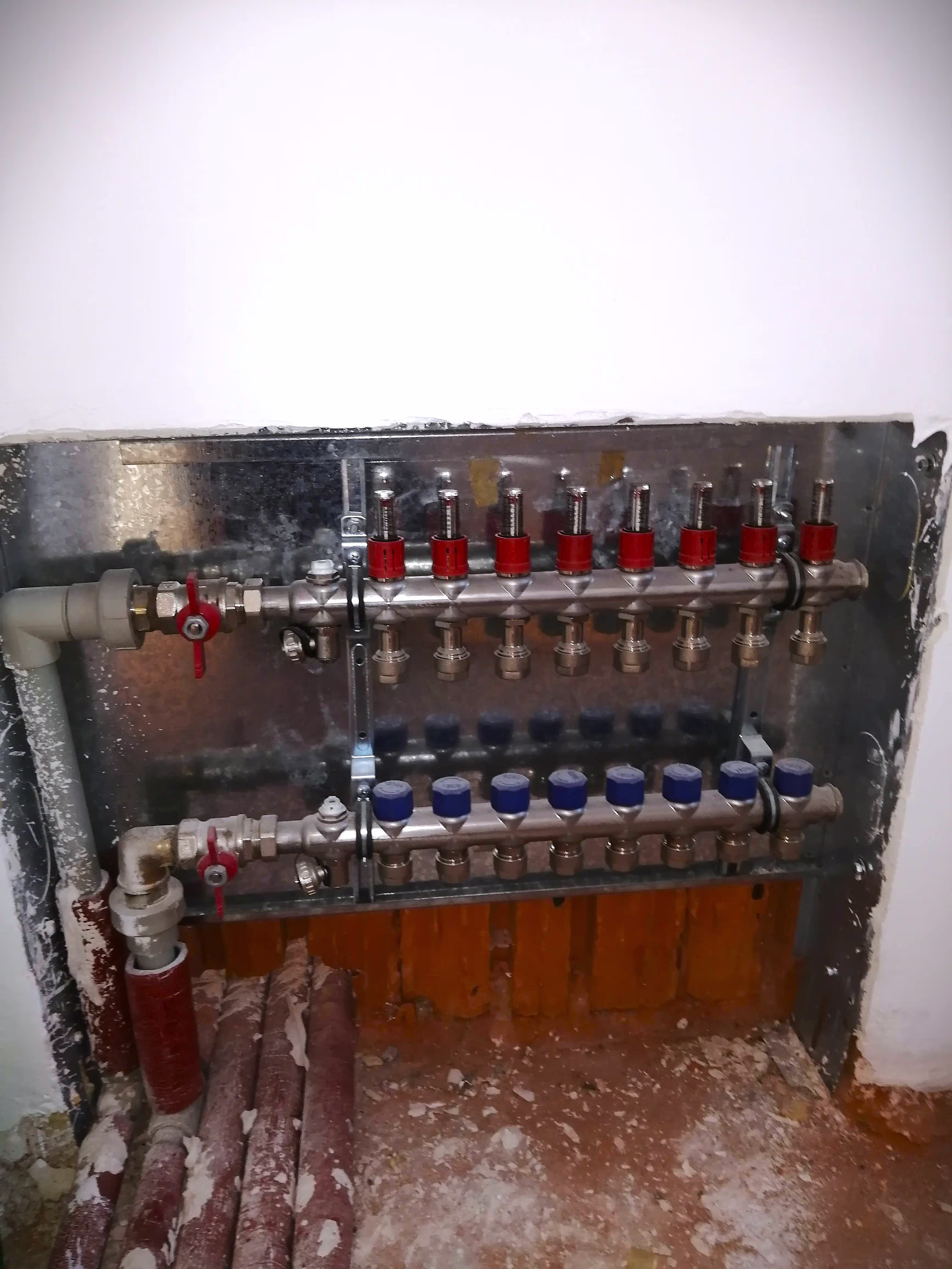 A heating distribution panel embedded in a wall, featuring multiple red and blue valve controls for water flow regulation.