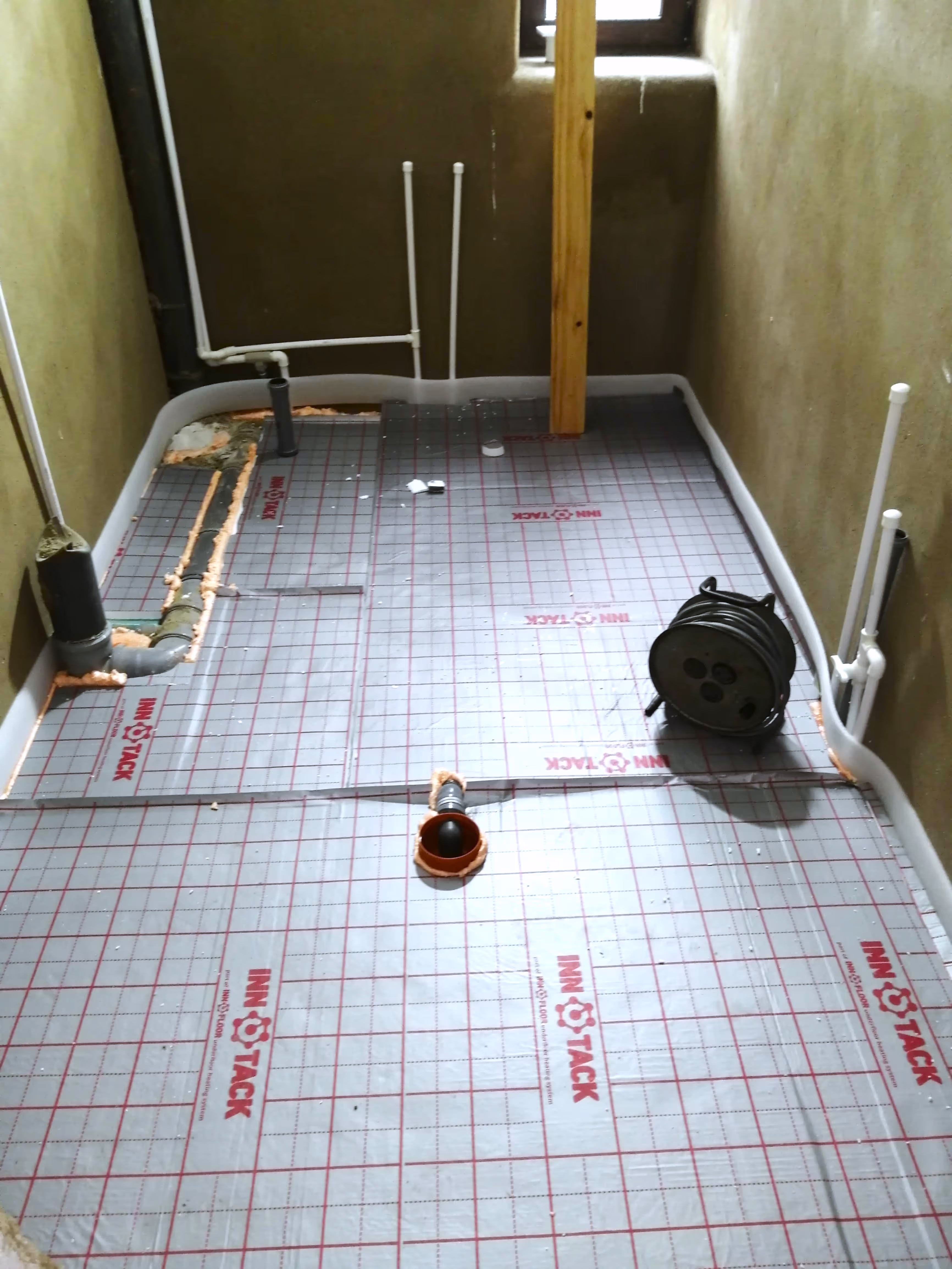 A room with underfloor heating insulation installed, featuring marked grid lines and visible plumbing connections.