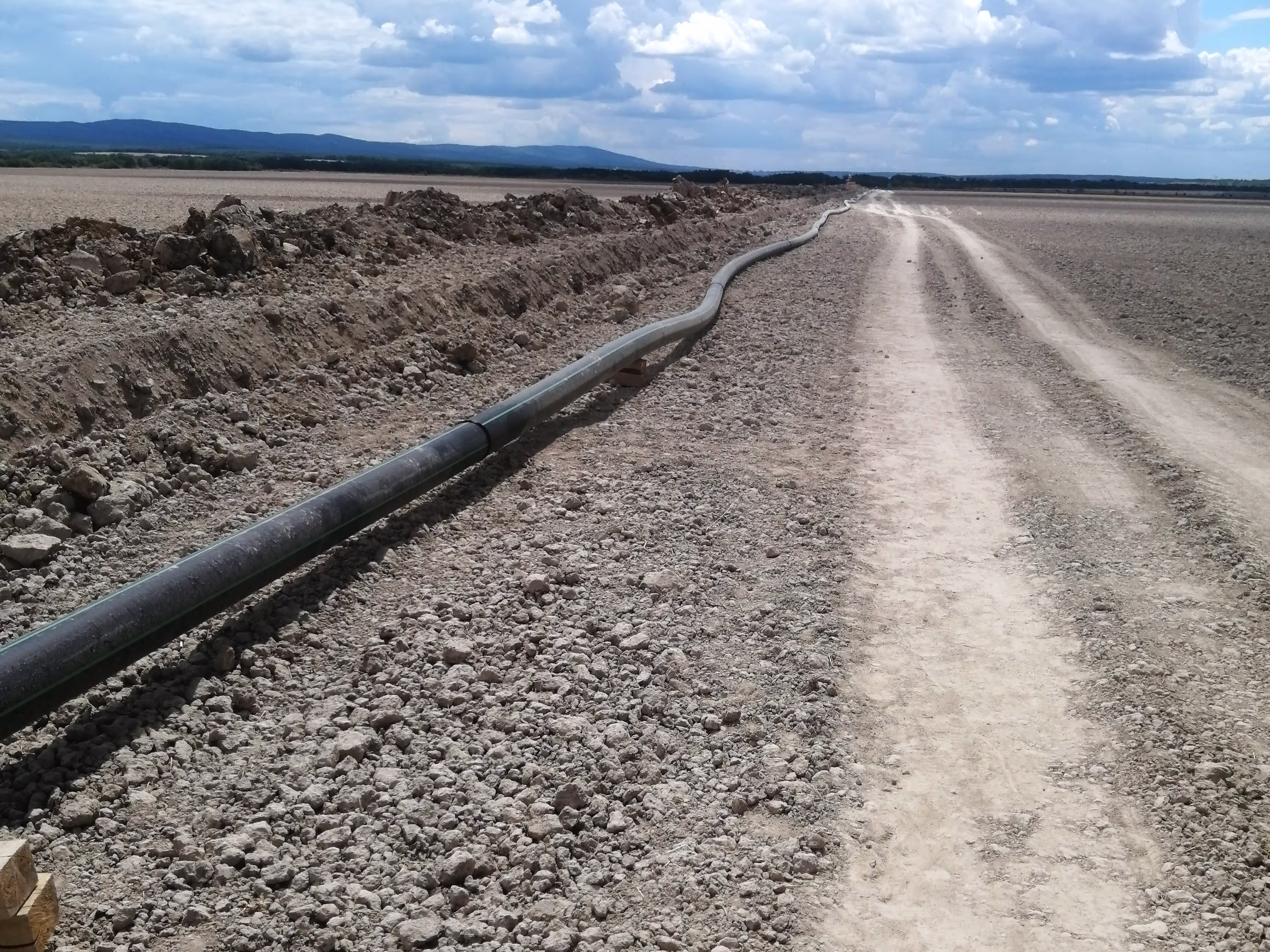 A long irrigation or drainage pipeline placed beside a dirt road, stretching far into the distance.