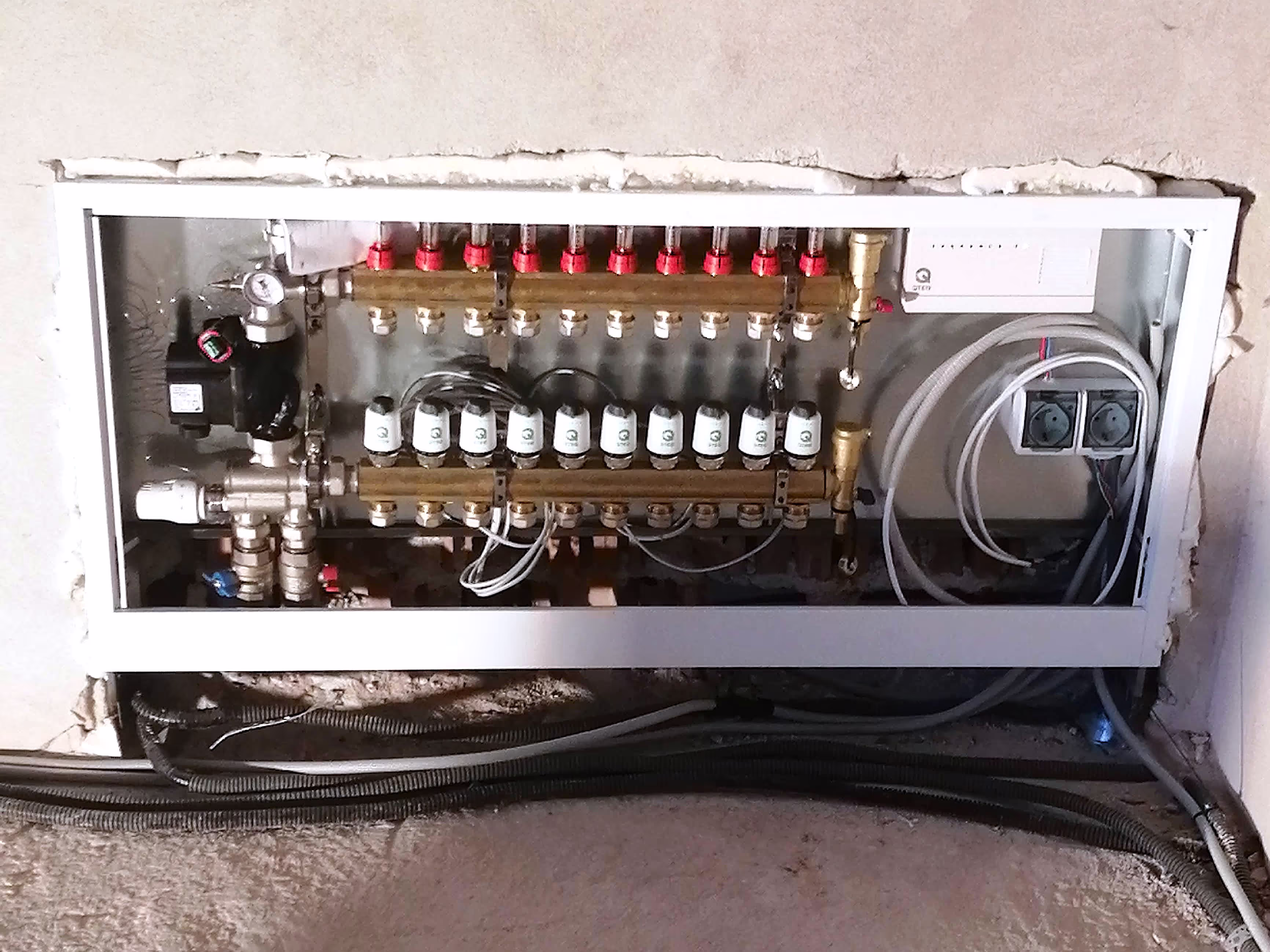 A detailed view of a built-in plumbing manifold system with red and white control valves and an integrated electronic control unit.