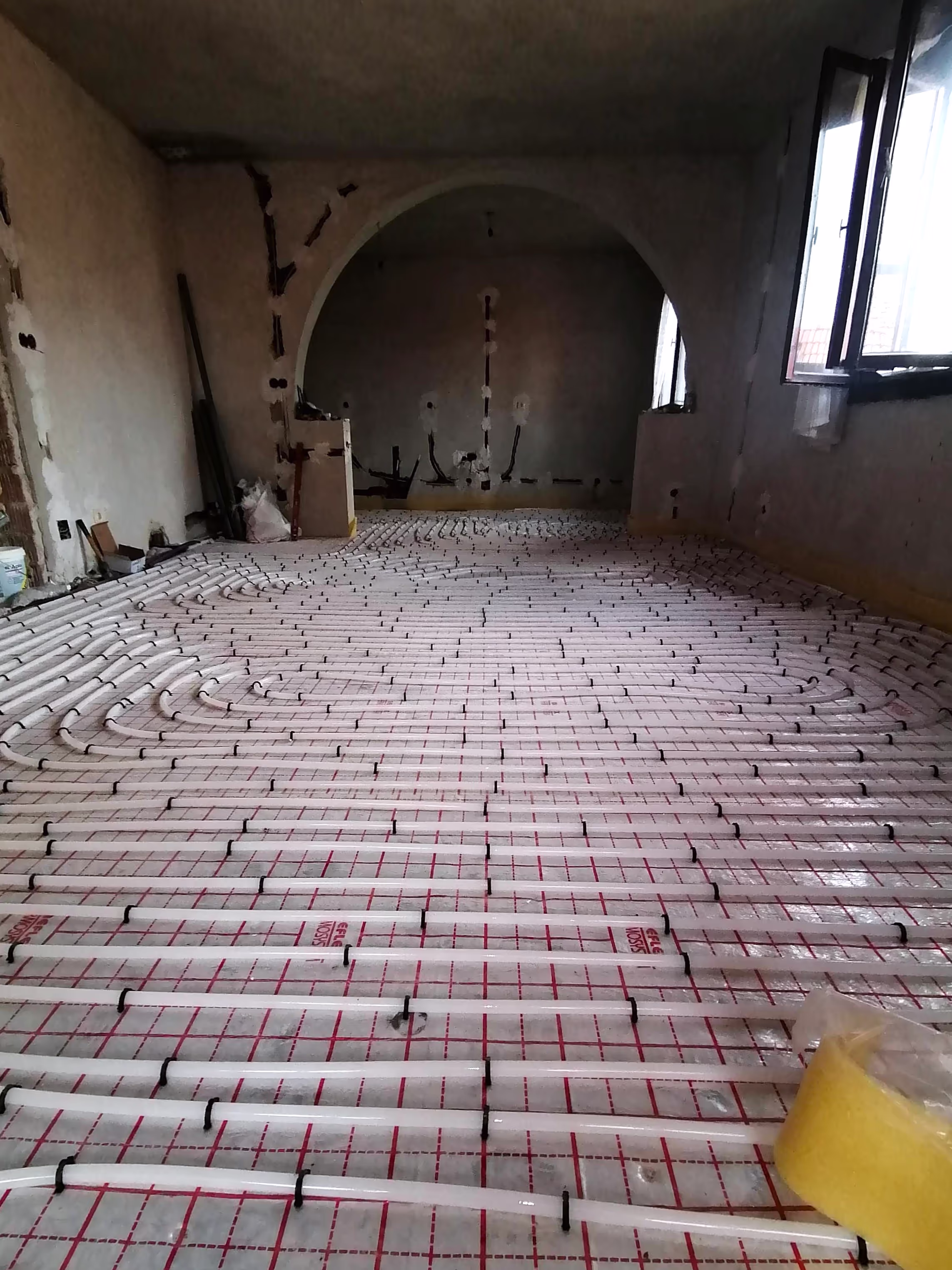 A room with underfloor heating pipes installed in a structured pattern on an insulating layer, ready for a concrete floor to be poured.